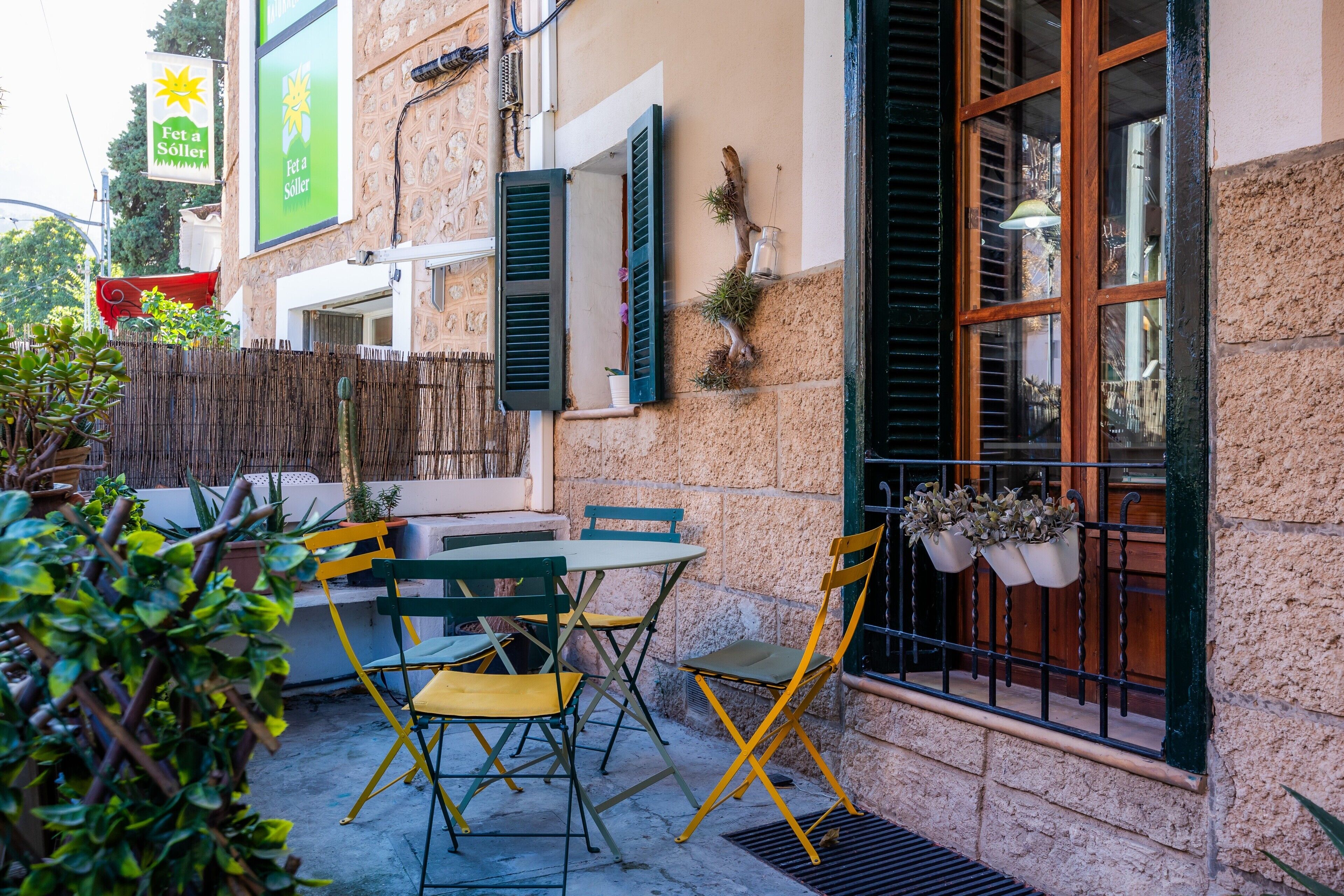 An outdoor seating area with a table and chairs, a window with shutters, and a sign above.