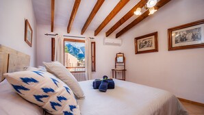 Un dormitori amb un llit gran, bigues de fusta, una finestra amb vistes i quadres emmarcats a la paret.