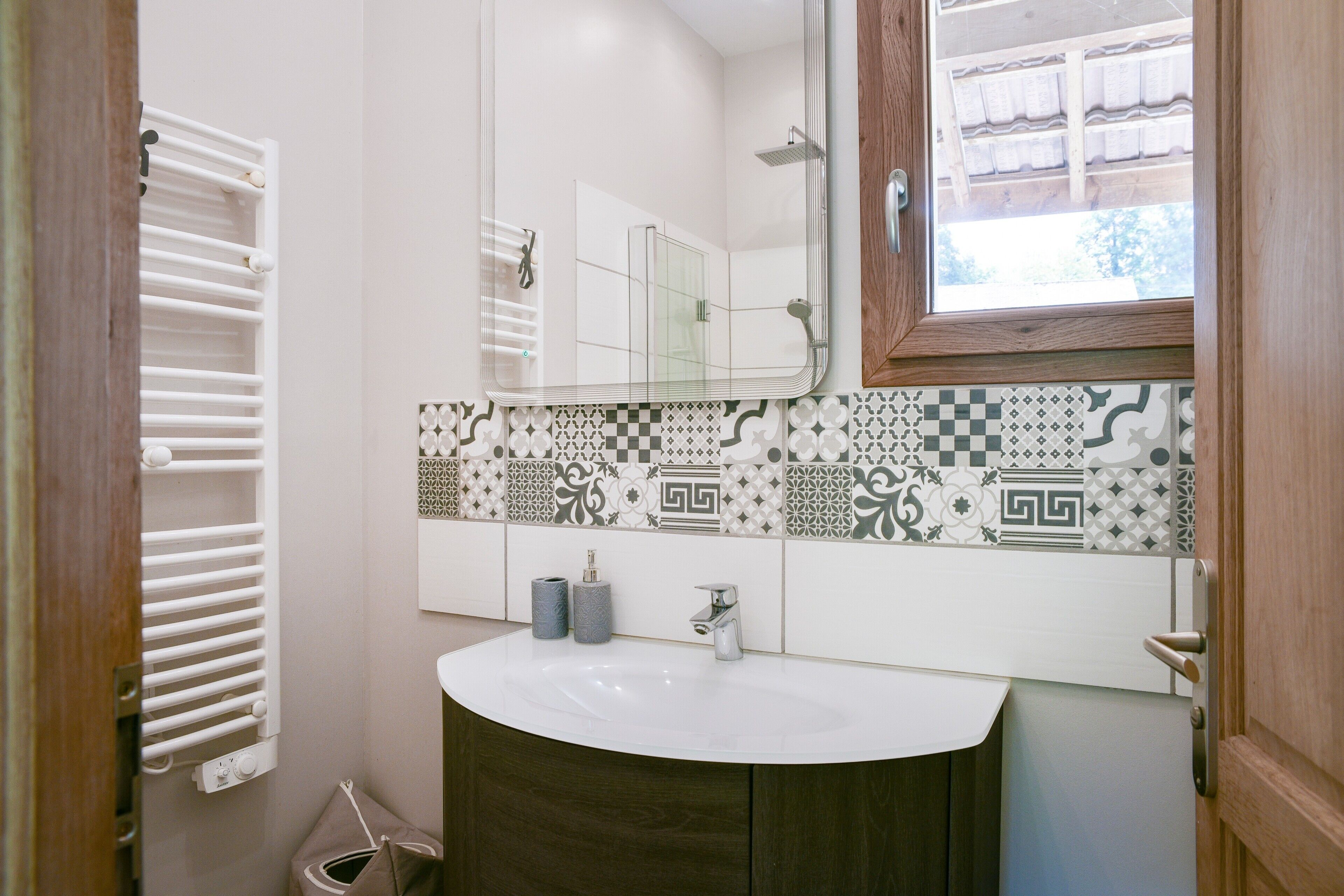 A bathroom with a white sink, a mirror, a towel rack, and patterned tiles.