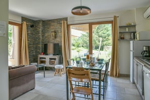 A living room with a sofa, a TV, a dining table with chairs, and a kitchen area with a fridge and microwave.