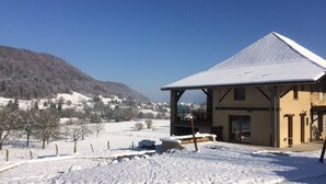 Un bâtiment enneigé doté d’un balcon, entouré d’un paysage hivernal et avec une montagne en arrière-plan.