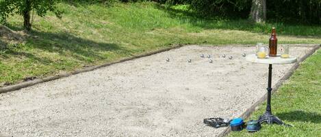 A croquet field with a table, balls, and a bottle.