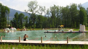 Une piscine dotée d’une terrasse en bois, entourée d’arbres et avec une montagne en toile de fond.