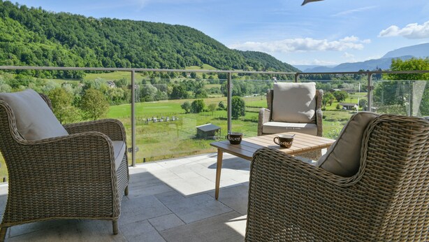 Un balcon agrémenté de meubles en osier, d’une table et offrant une vue sur un paysage verdoyant.