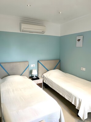 A hotel room with two beds, a nightstand with a lamp, an air conditioning unit, and a wall-mounted light switch. - Holiday Home 'Mateu' with Private Pool, Wi-Fi and Air Conditioning (Colonia de Sant Pere)