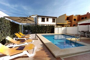 A swimming pool with lounge chairs and umbrellas, surrounded by buildings. - Holiday Home 'Mateu' with Private Pool, Wi-Fi and Air Conditioning (Colonia de Sant Pere)