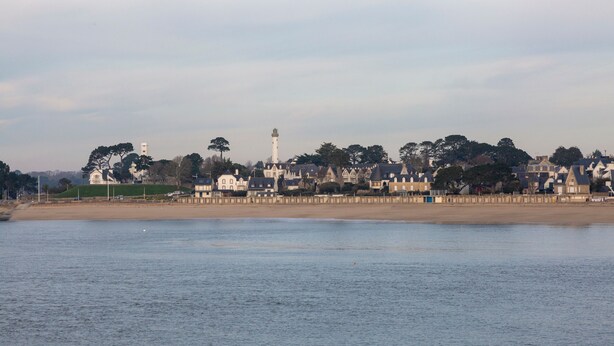 Une ville côtière qui se distingue par son phare imposant, sa plage de sable et une rangée de maisons traditionnelles.