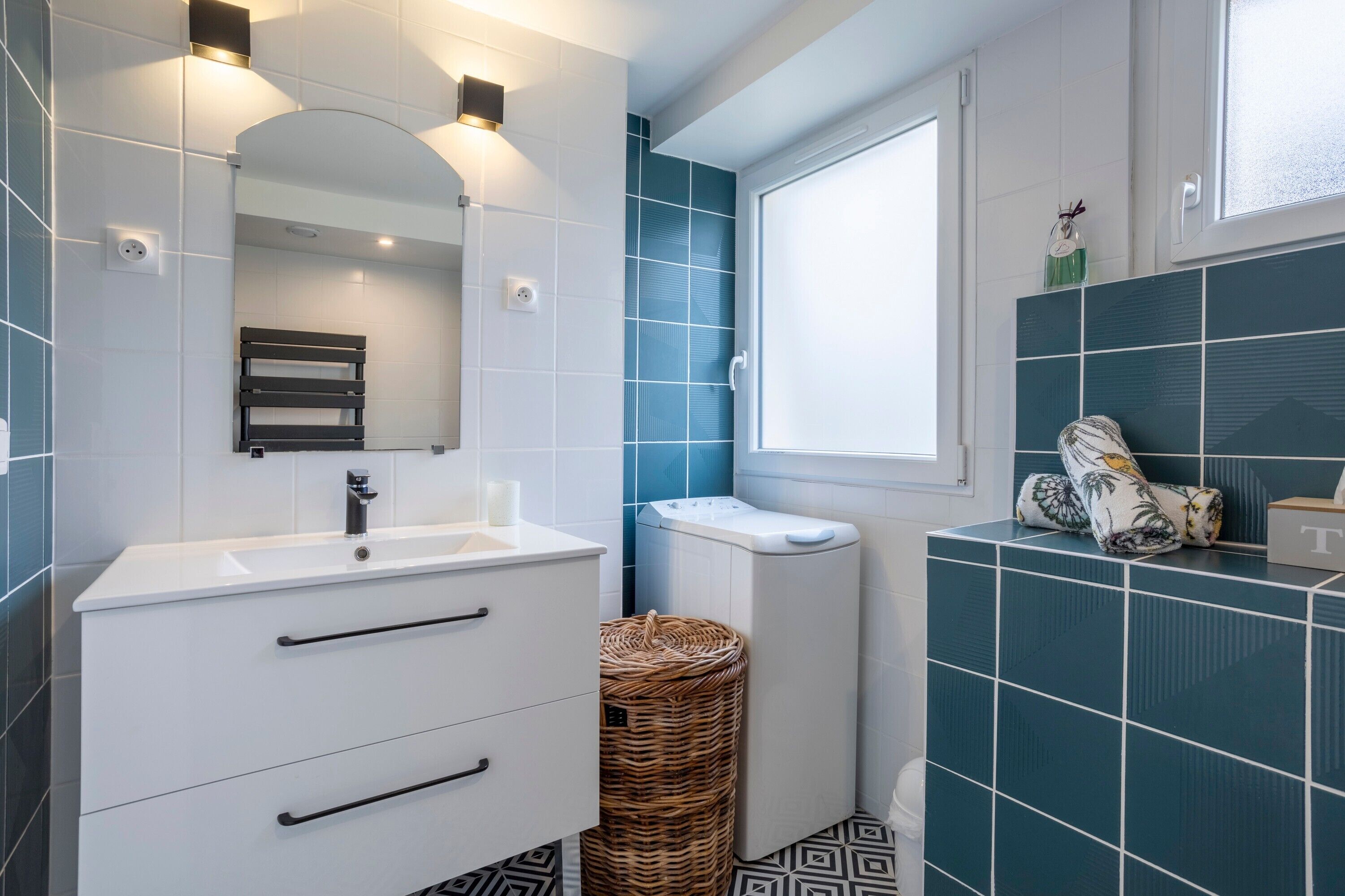 Een moderne badkamer met witte en blauwe tegels, een wit wastafelmeubel, een spiegel en een raam.
