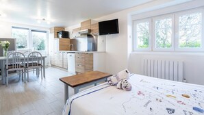 Une cuisine moderne dotée d’une cuisinière intégrée, un coin repas avec une table et des chaises, et une grande fenêtre donnant sur les arbres.