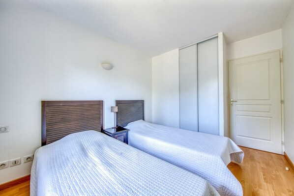 A bedroom with two beds, a bedside table with a lamp, a wardrobe, and a door.