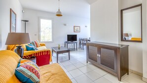 A living room with a sofa, a TV, a dining table, and a cabinet. - Accessible Apartment for Persons with Reduced Mobility with Garden and Shared Pool in Soulac-sur-Mer (Soulac-sur-Mer)