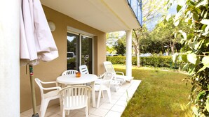 A patio with a table and chairs, a covered area, and a view of a garden and street. - Accessible Apartment for Persons with Reduced Mobility with Garden and Shared Pool in Soulac-sur-Mer (Soulac-sur-Mer)