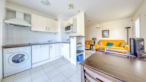 A modern kitchen with a built-in washing machine, a dining area with a yellow sofa, and a compact living space. - Accessible Apartment for Persons with Reduced Mobility with Garden and Shared Pool in Soulac-sur-Mer (Soulac-sur-Mer)