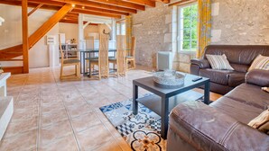 Un grand espace de vie comprenant un canapé en cuir marron, une table à manger avec des chaises, et une cuisine en arrière-plan.