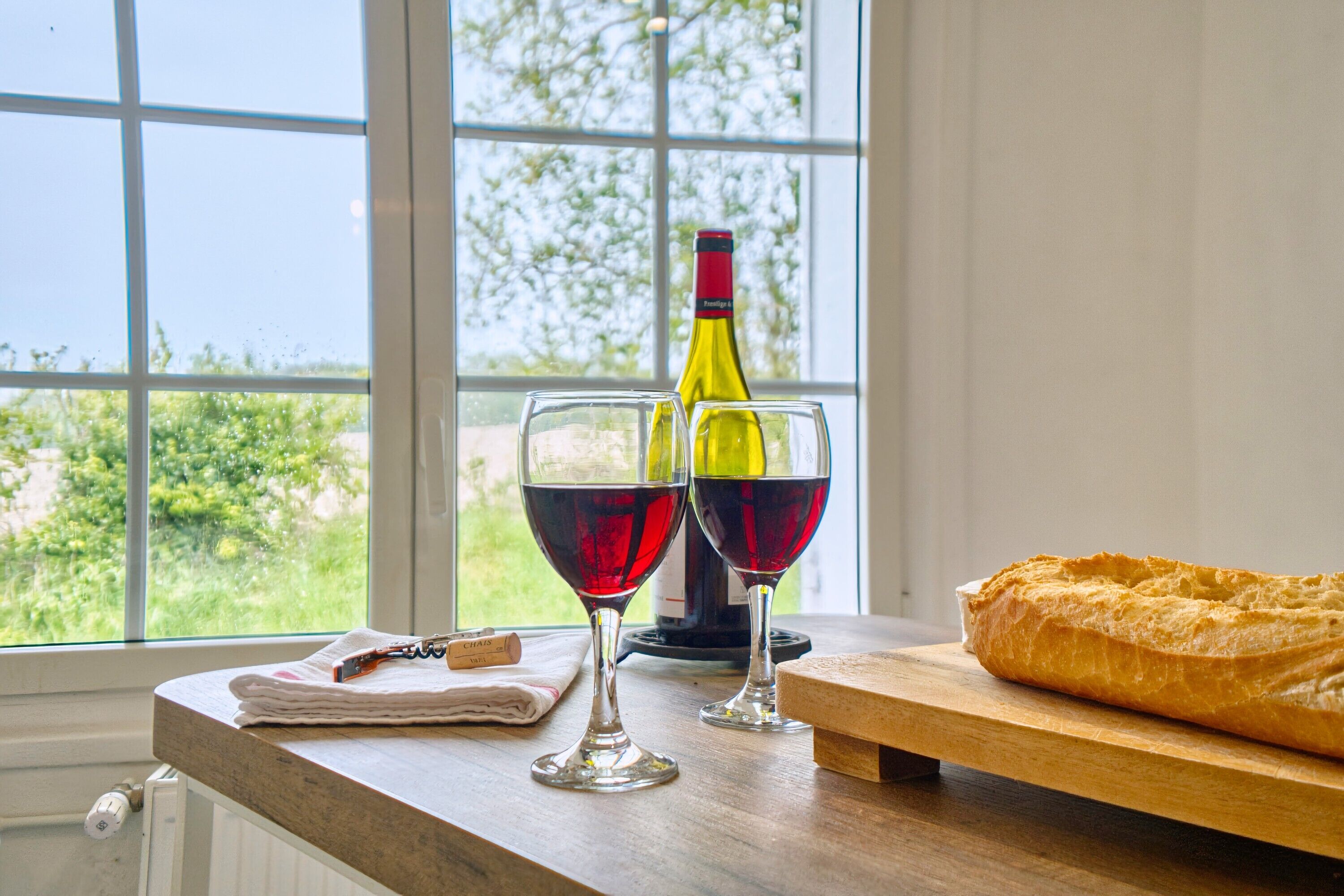 Una mesa con dos copas de vino, una botella y una hogaza de pan.