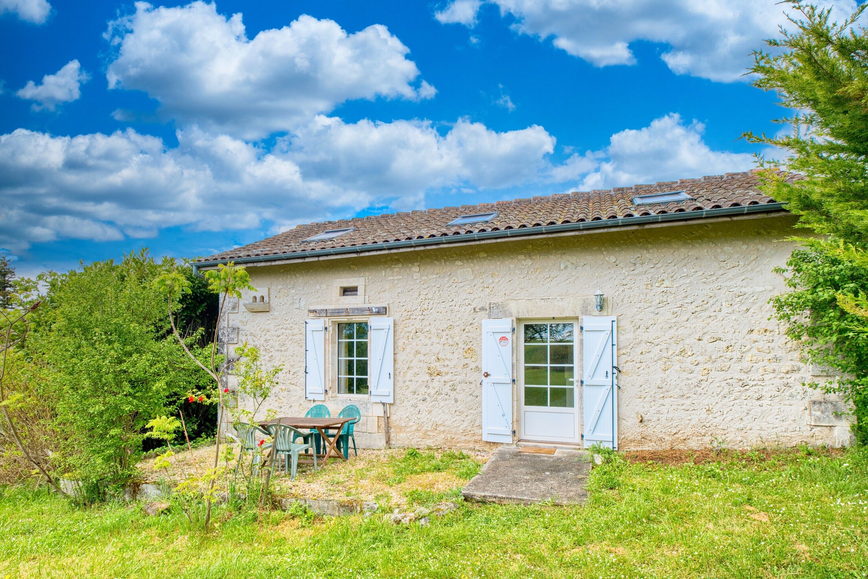 A rustic stone building with a tiled roof, a small porch, and a table with chairs outside.