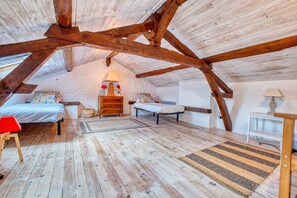 Une chambre située dans un espace de type « loft », avec des poutres en bois apparentes, un lit, un bureau et une chaise.
