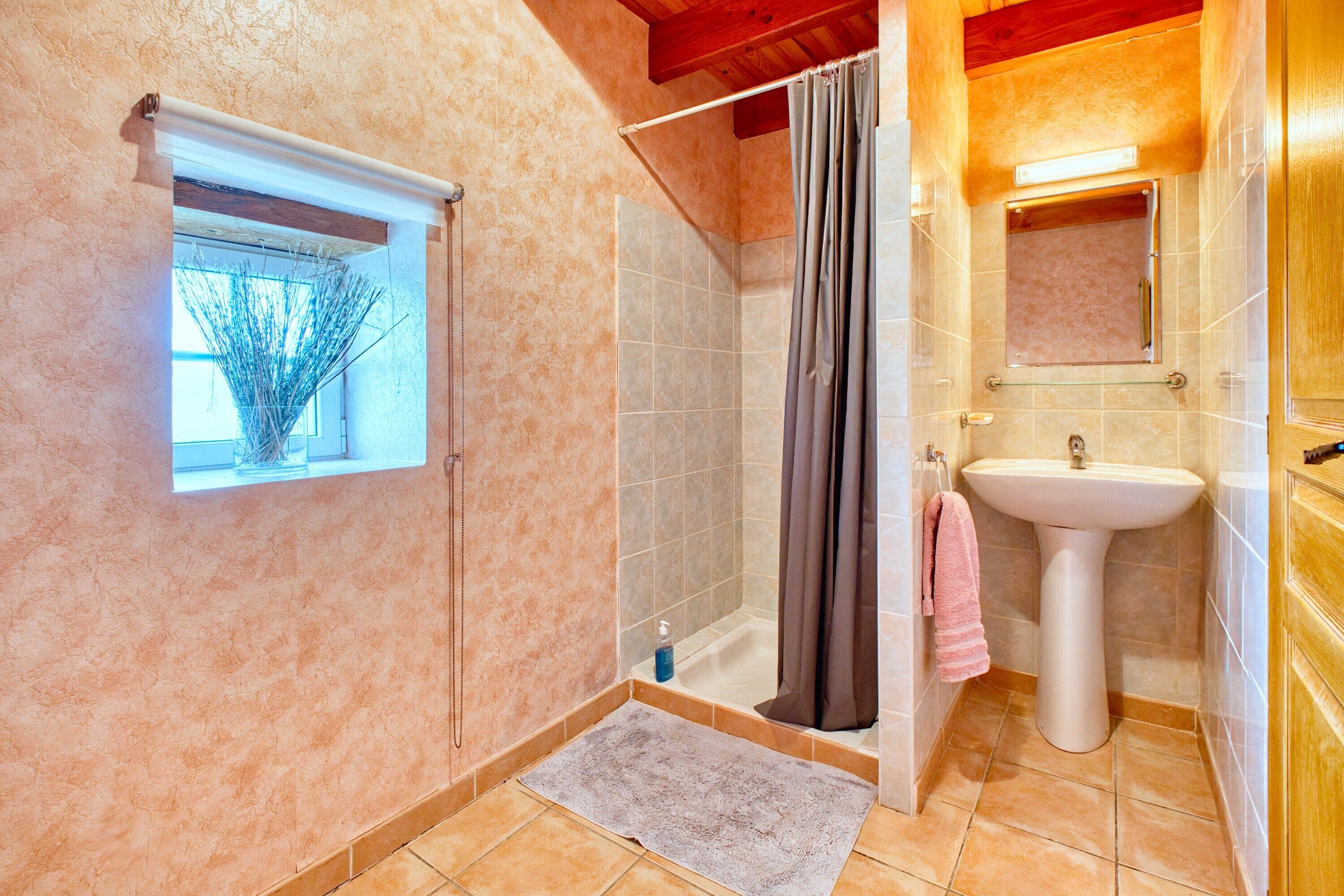 Un baño con ducha, lavamanos, ventana con vistas y un perchero para toallas.