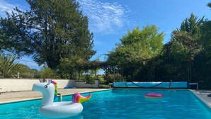 Une piscine avec des bouées en forme de licorne gonflable, entourée d’arbres et sous un ciel dégagé.