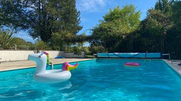 Una piscina con flotadores de unicornio inflables, rodeada de árboles y un cielo despejado.