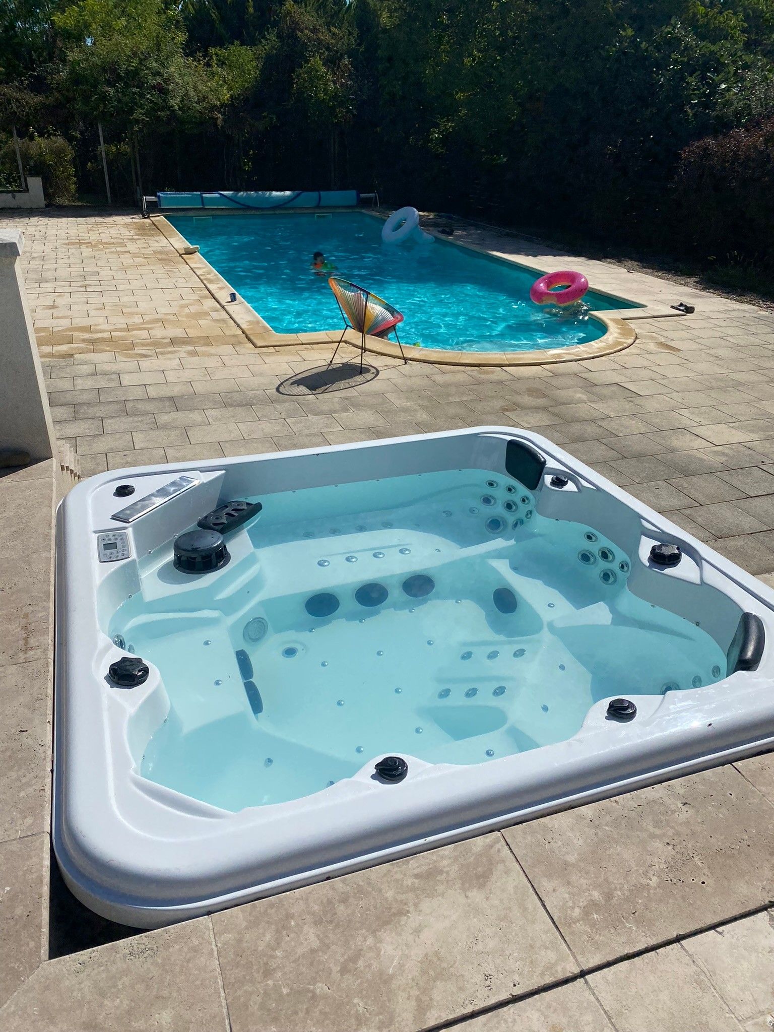 Ein Whirlpool mit Bedienfeld, ein Schwimmbecken mit einem Schwimmreifen und ein Stuhl am Pool.
