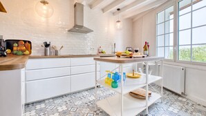 A modern kitchen with white cabinetry, a patterned tile floor, a wooden countertop, and a window with a view. - Charming Stone House with Pool and Enclosed Garden :
A Haven of Comfort and Serenity (Allemans)