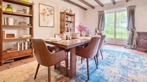 A dining area with a wooden table, chairs, bookshelves, and a window with curtains. - Charming Stone House with Pool and Enclosed Garden :
A Haven of Comfort and Serenity (Allemans)