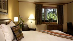 Een hotelkamer met een bed, twee bedlampjes, een stoel, een raam met gordijnen, en een lijst aan de muur.