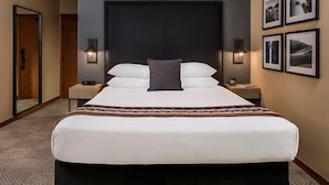 A hotel room with a large bed, two bedside tables, a headboard, and framed pictures on the wall. - Premier King Room with Fireplace and Forest Views (Stevenson)