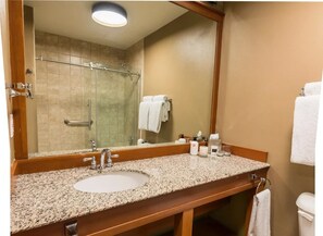 A bathroom with a granite countertop sink, a large mirror, a glass shower enclosure, and a towel rack. - Premier Double Room with Forest Views (Stevenson)