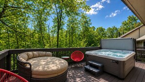 Une terrasse avec un jacuzzi, un canapé rond en osier et une chaise rouge.