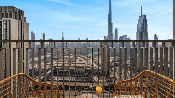 Un balcon avec des fauteuils en osier, une table sur laquelle se trouve un panier de fruits et une boisson, et une vue sur le paysage urbain, notamment le Burj Khalifa.