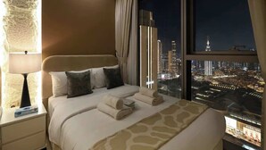 Une chambre d’hôtel moderne avec un grand lit, une table de chevet, une lampe et une vue sur le paysage urbain illuminé la nuit.