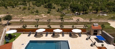 A pool area with a stone deck, lounge chairs, and umbrellas.