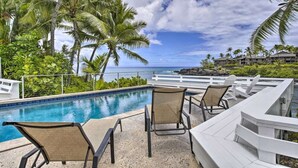 A pool area with lounge chairs and a view of the ocean.