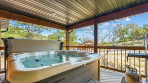 A hot tub on a wooden deck with a view of trees and a clear sky.