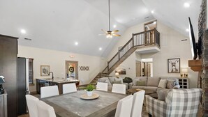 A spacious living area with a dining table, comfortable seating, a staircase to an upper level, and a kitchen area.