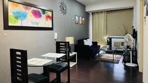 Uma sala de estar moderna com uma mesa de jantar de vidro, sofás pretos e um quadro abstrato colorido.