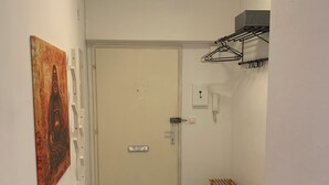 Een gang met een witte deur, een schilderij aan de muur, een telefoon en een droogrek.