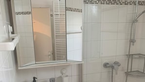 Een badkamer met een wit wastafelmeubel, spiegel en douche.