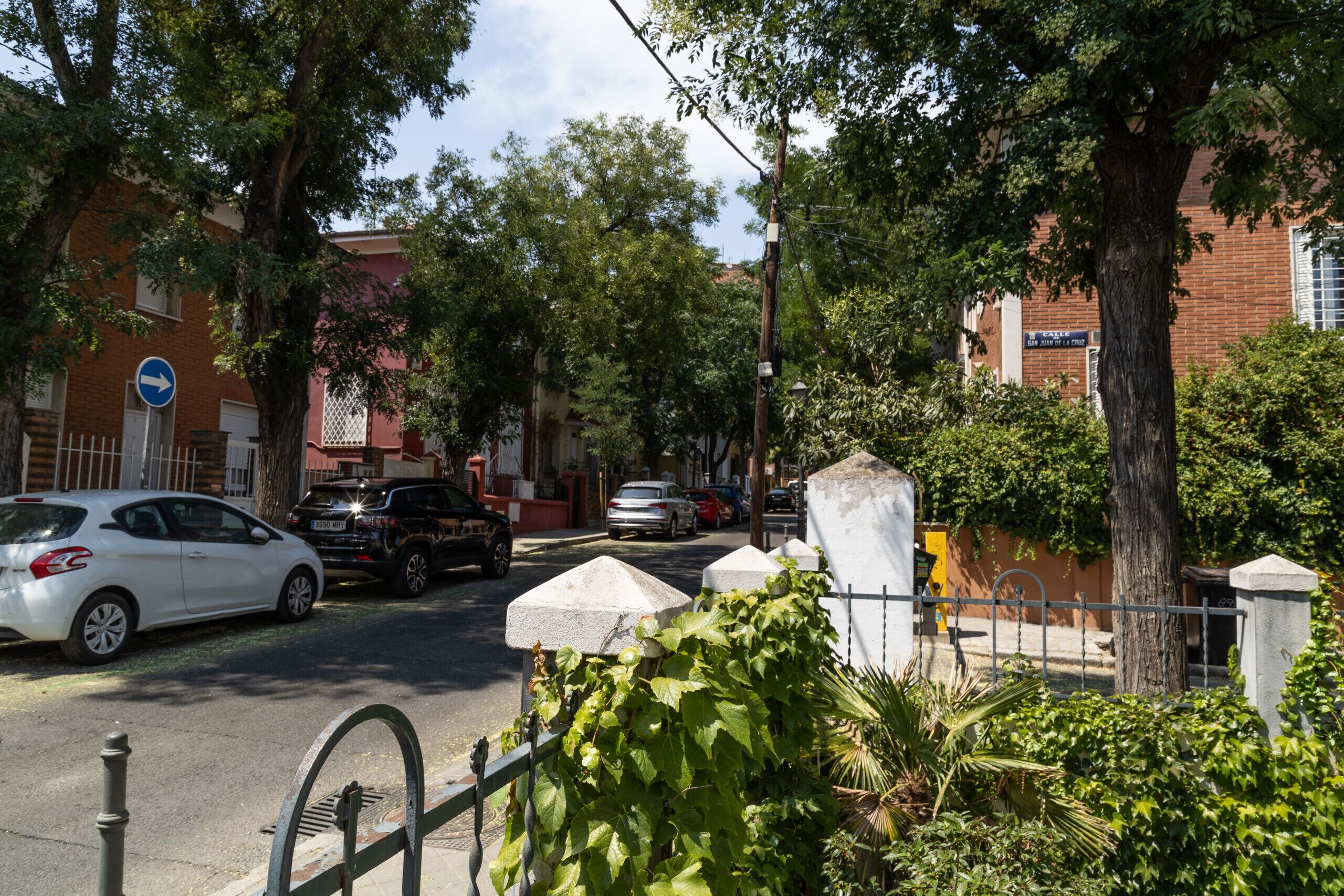 Una calle con coches aparcados, árboles y un edificio de fachada de ladrillo rojo.