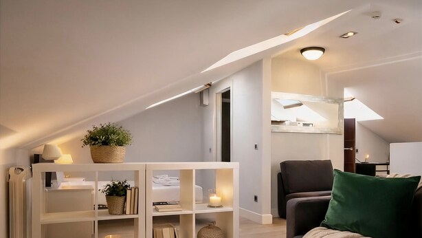 A modern loft apartment with a high ceiling, built-in white shelving unit, a dark leather sofa, and a wooden coffee table.
