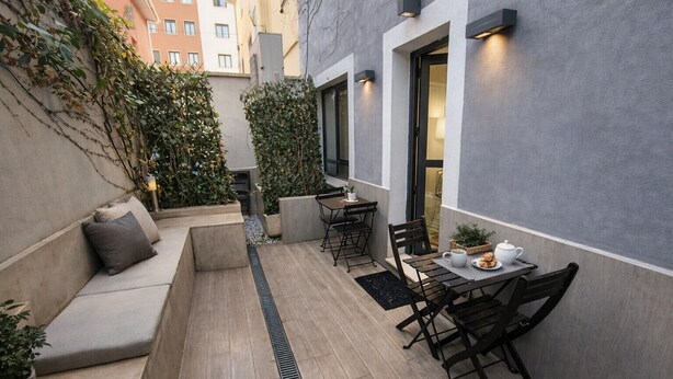 Un pequeño patio al aire libre con un sofá, una mesa con sillas y plantas en macetas.
