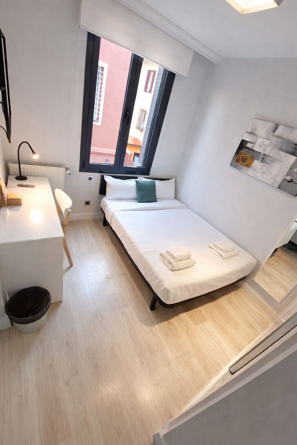 A small, modern room with a bed, a desk, and a window.
