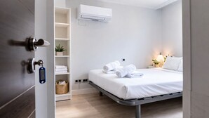 Una habitación de hotel moderna con cama, estante empotrado con toallas, aire acondicionado de pared y lámpara de noche.