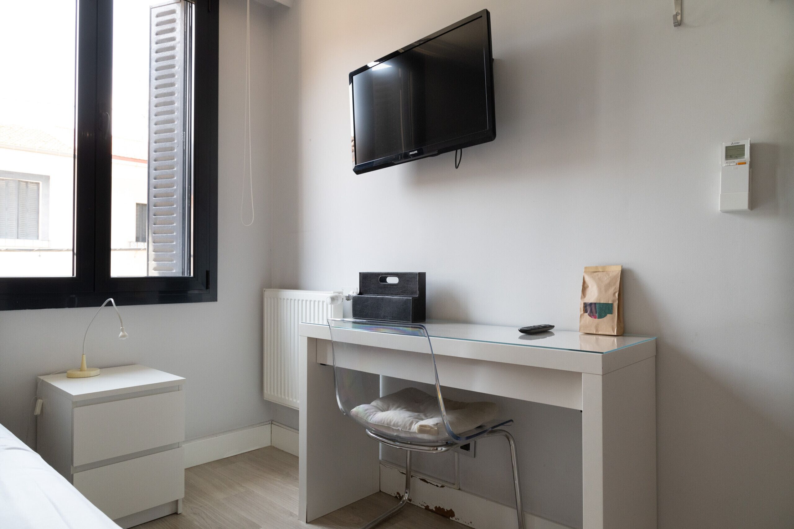 Una camera moderna con un letto, una scrivania con un computer, una televisione e una finestra con persiane.
