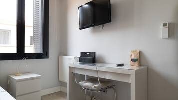 Una camera moderna con un letto, una scrivania con un computer, una televisione e una finestra con persiane.