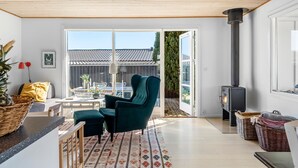 A modern living room with a large window, a green armchair, a wooden ceiling, and a fireplace. - 2 bedroom cozy home in Kerteminde (Kerteminde)