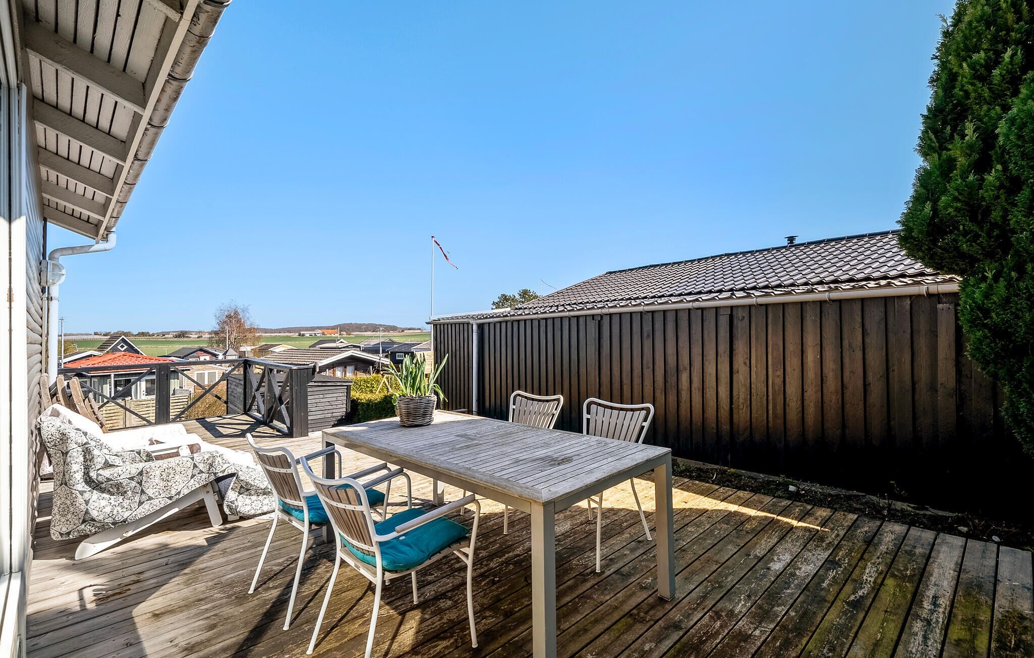 Una terraza de madera con una mesa y sillas, una cerca de madera y vistas del entorno.