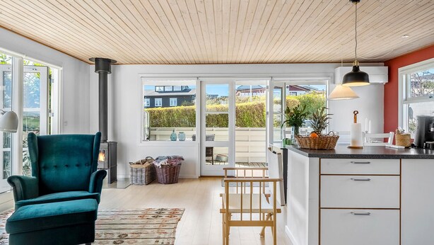 A modern kitchen with a wooden ceiling, a teal armchair, and a view of the outside through large windows. - 2 bedroom cozy home in Kerteminde (Kerteminde)